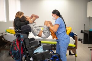 Nurse gently assisting a child into a wheelchair at Peek A Boo Pediatric Care, Hollywood, FL.