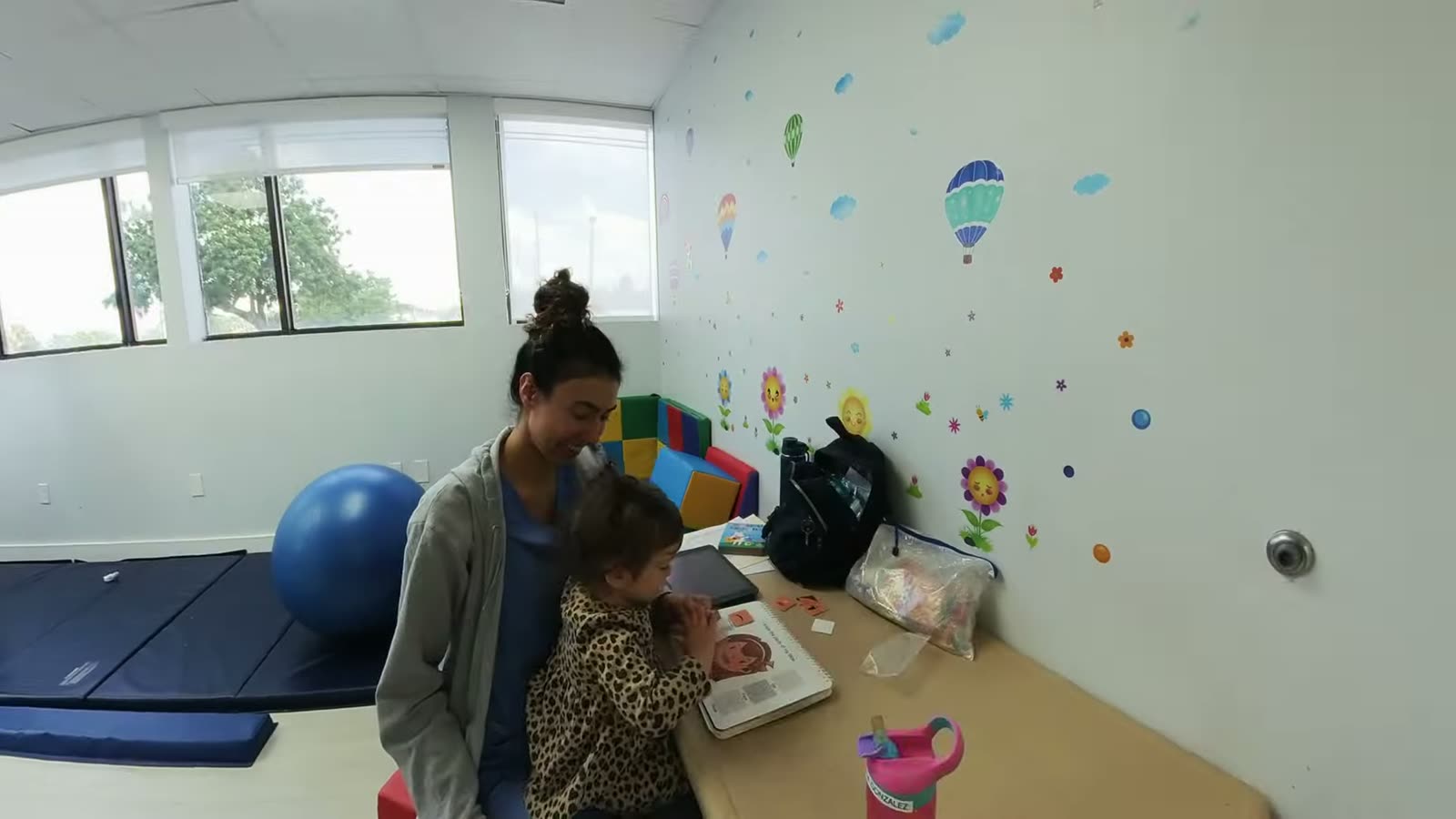 A caregiver working one-on-one with a young child in the therapy room at Peek A Boo PPEC, with floor mats and a therapy ball