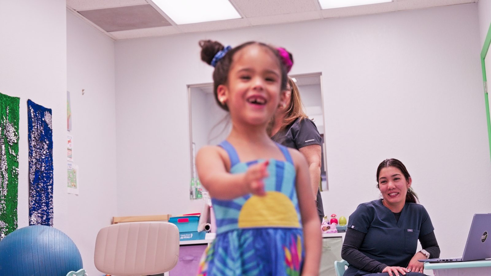 Young girl smiling and reaching toward the camera in the therapy gym at Peek A Boo Pediatric Care in Hollywood, FL
