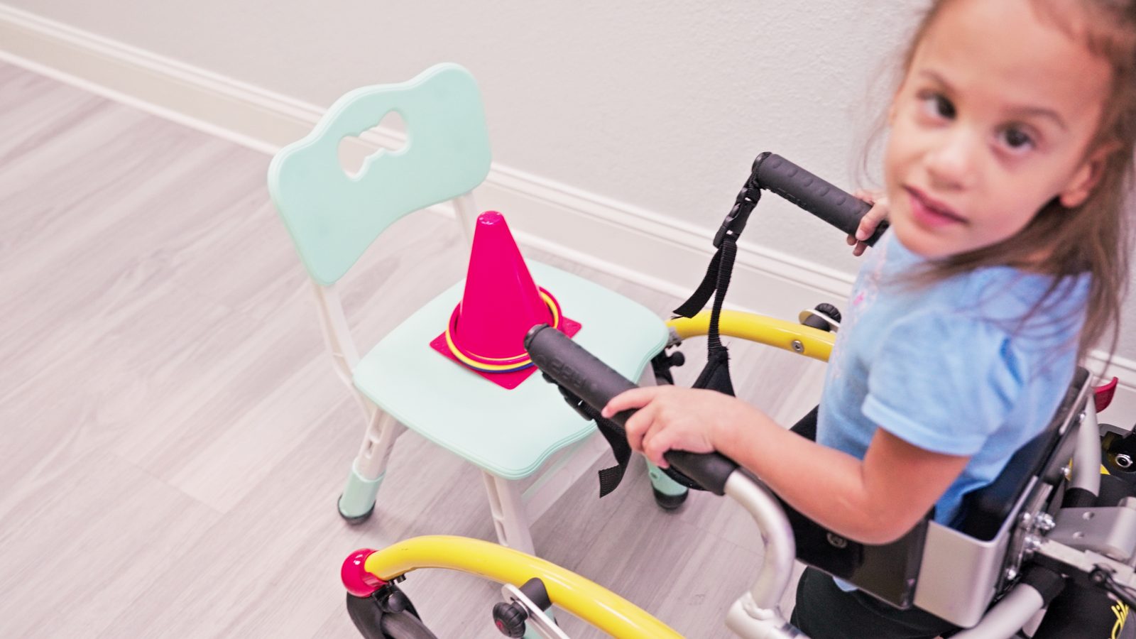 Young girl holding the handles of a gait trainer during therapy at Peek A Boo Pediatric Care in Hollywood, FL