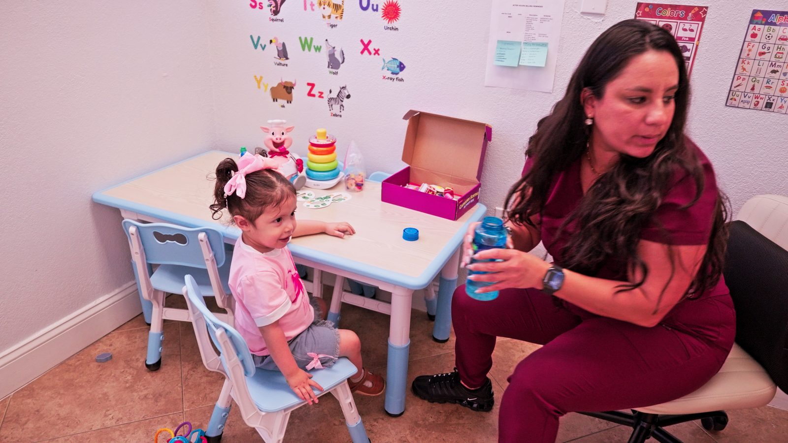Therapist working with a toddler at a small table in a bright therapy room at Peek A Boo Pediatric Care in Hollywood, FL